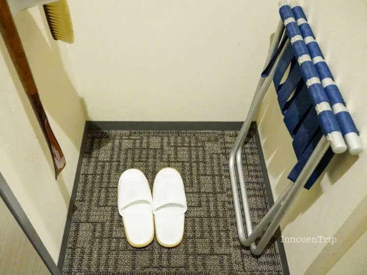 タオル地のスリッパと折り畳みバゲージラックが並ぶ玄関スペース